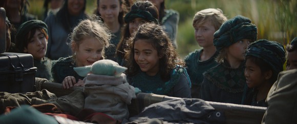 A group of children huddled around the Baby Yoda character.