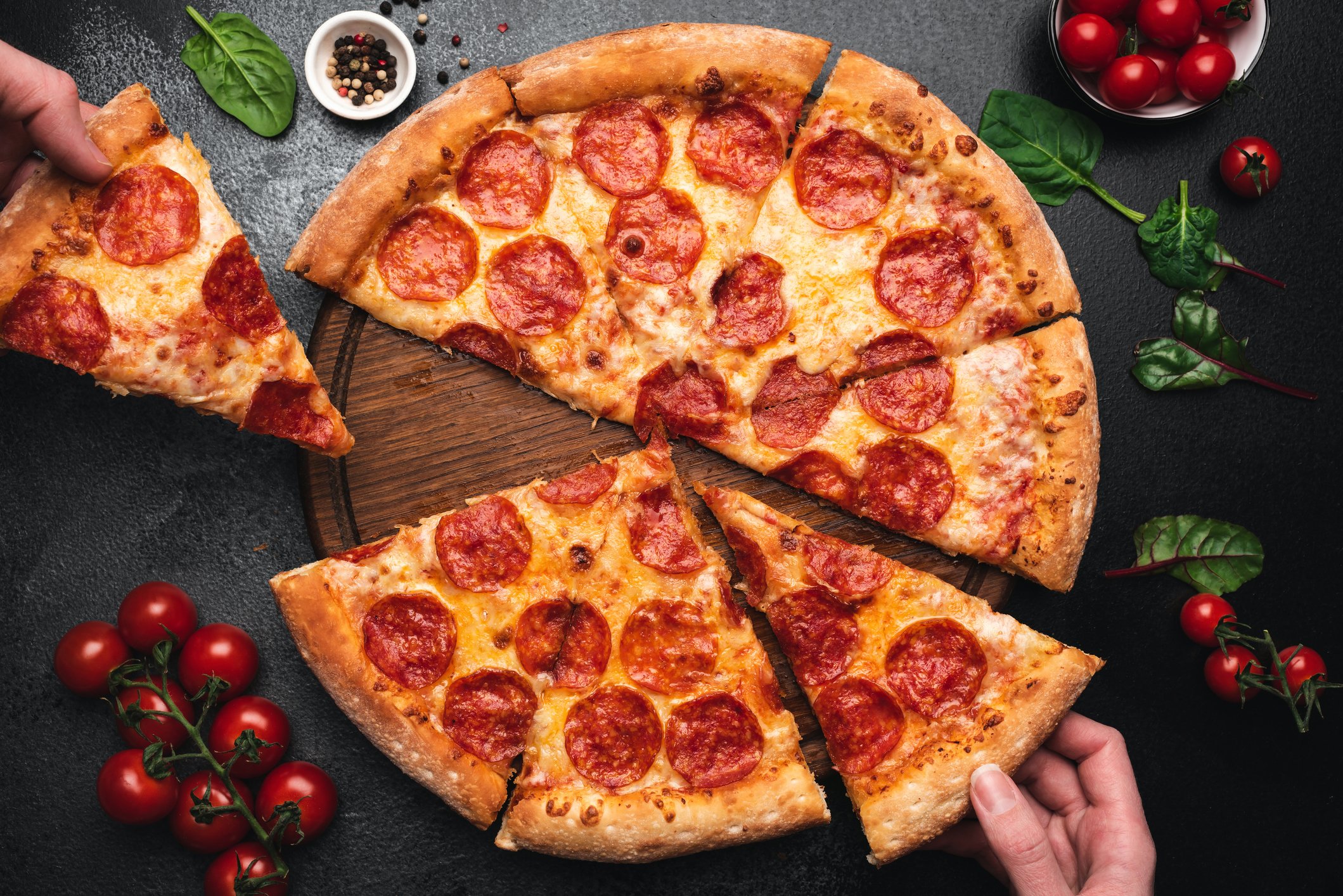 Two hands grabbing slices of pizza from a pie.