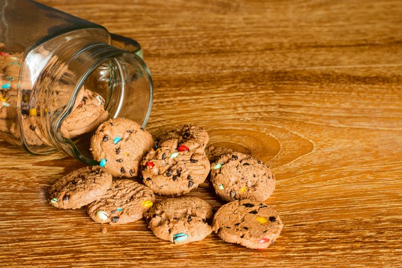 Cookies spilling out of a glass cookie jar onto a wooden table.