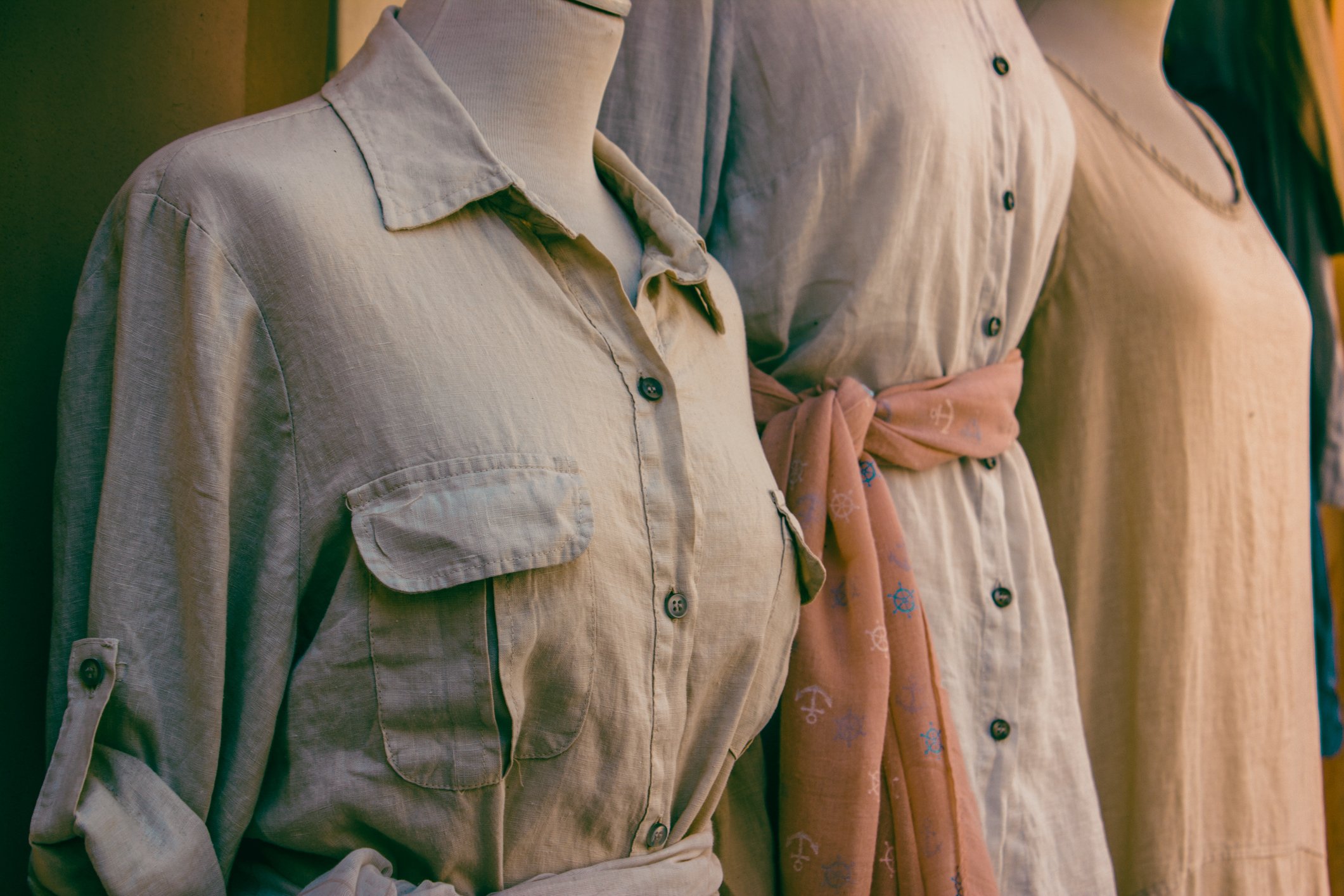 Three beige dresses are displayed on mannequins in a shop.
