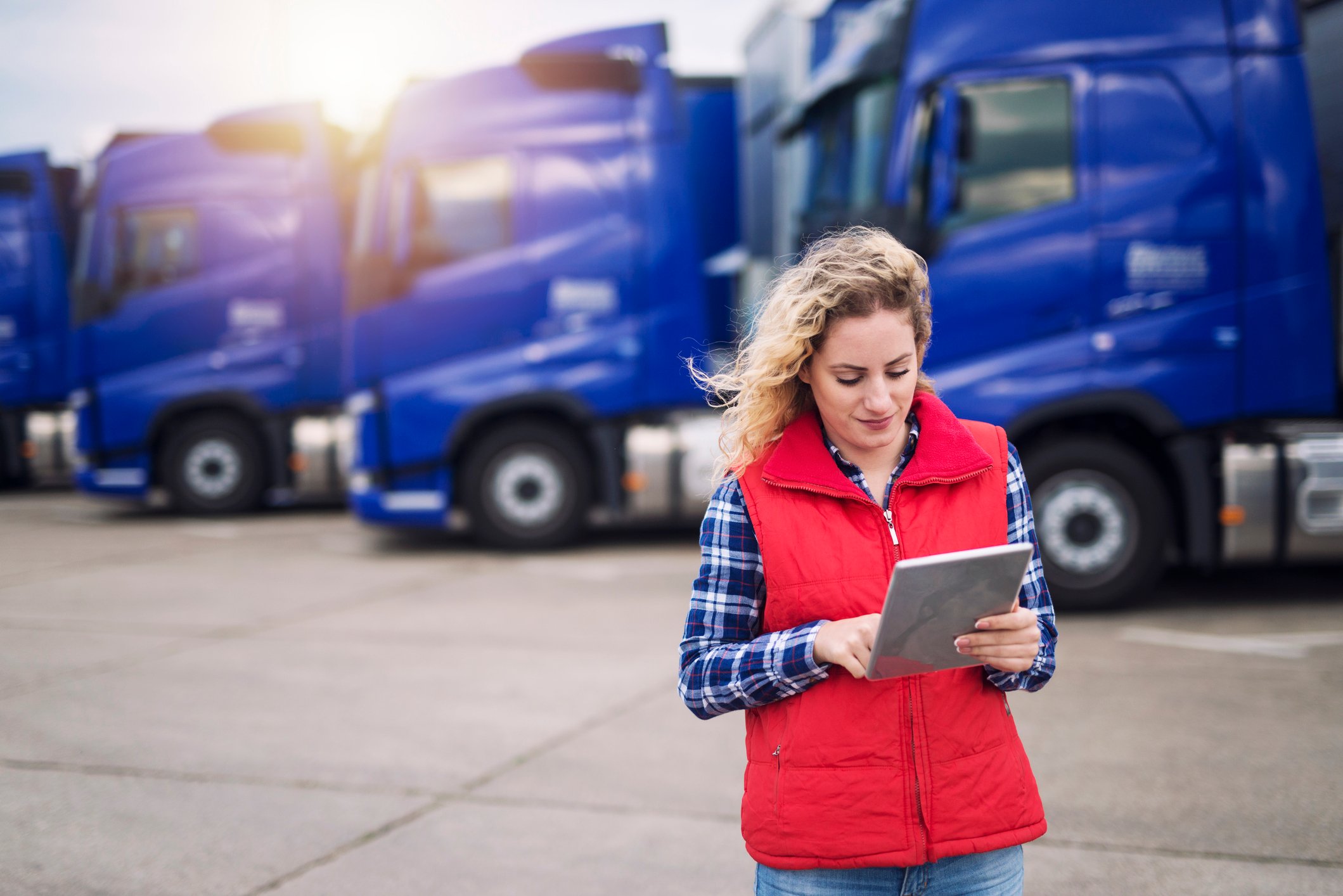 A woman using a tablet in front of a fleet of freight trucks