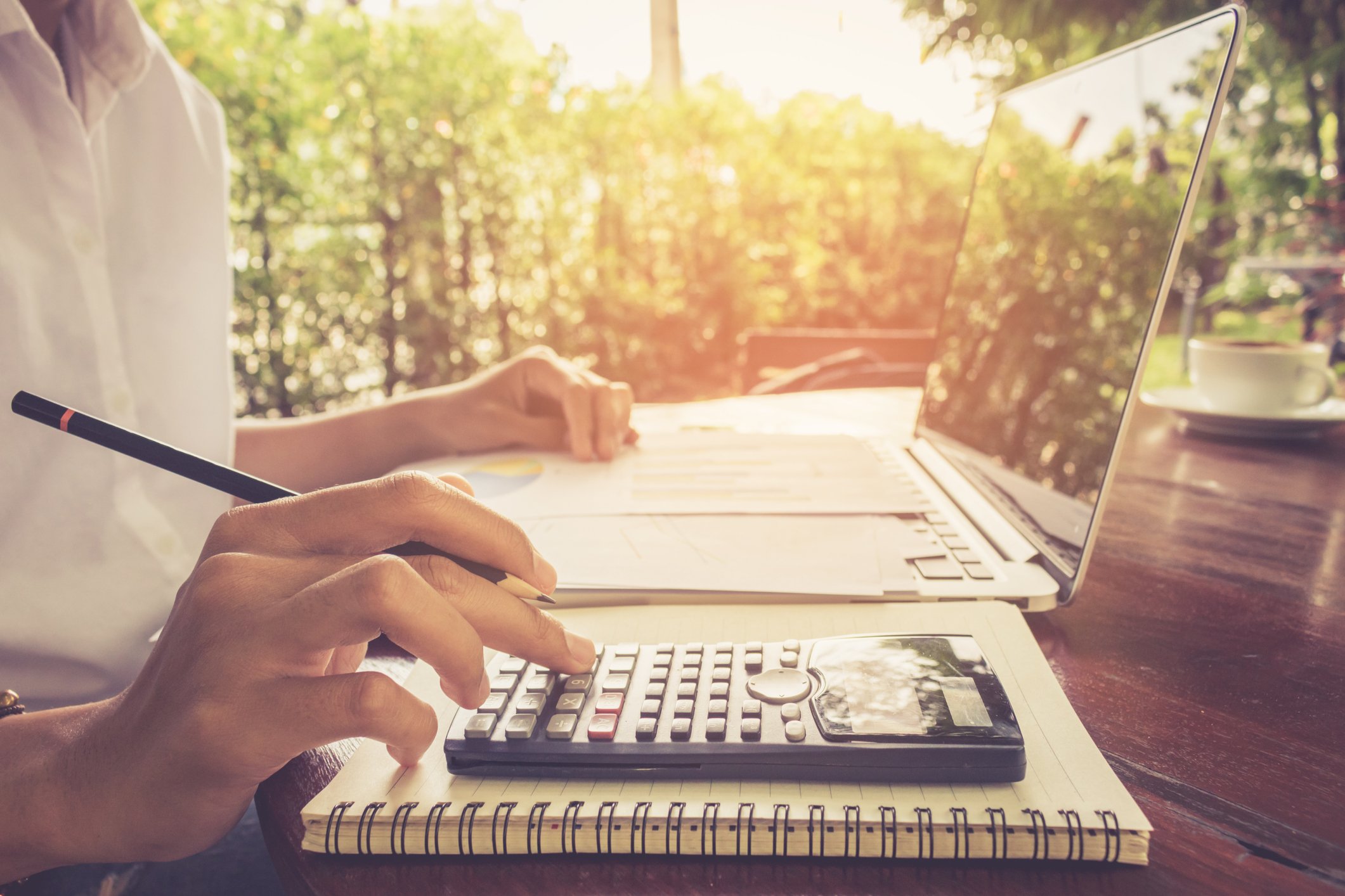 A man at outdoor desk, using a calculator with one hand a laptop with his left