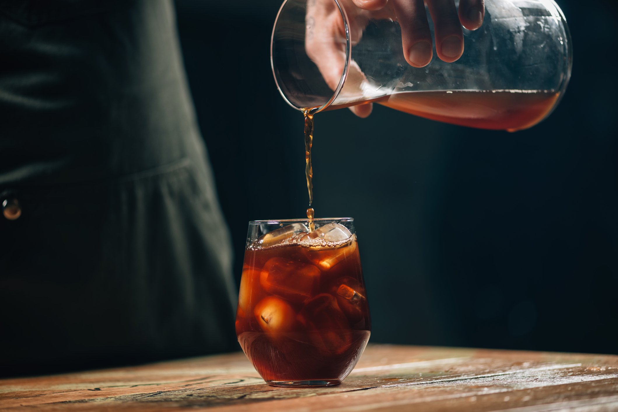 Photograph of hand pouring cold coffee into glass of ice