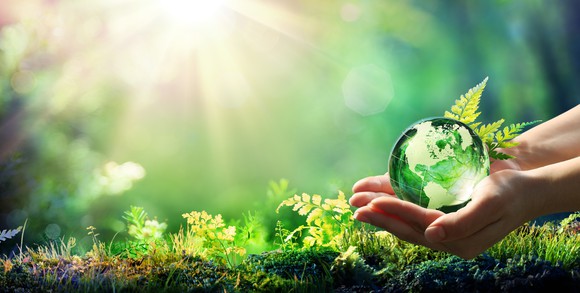 A green planet earth is held in hands in an outdoor setting.