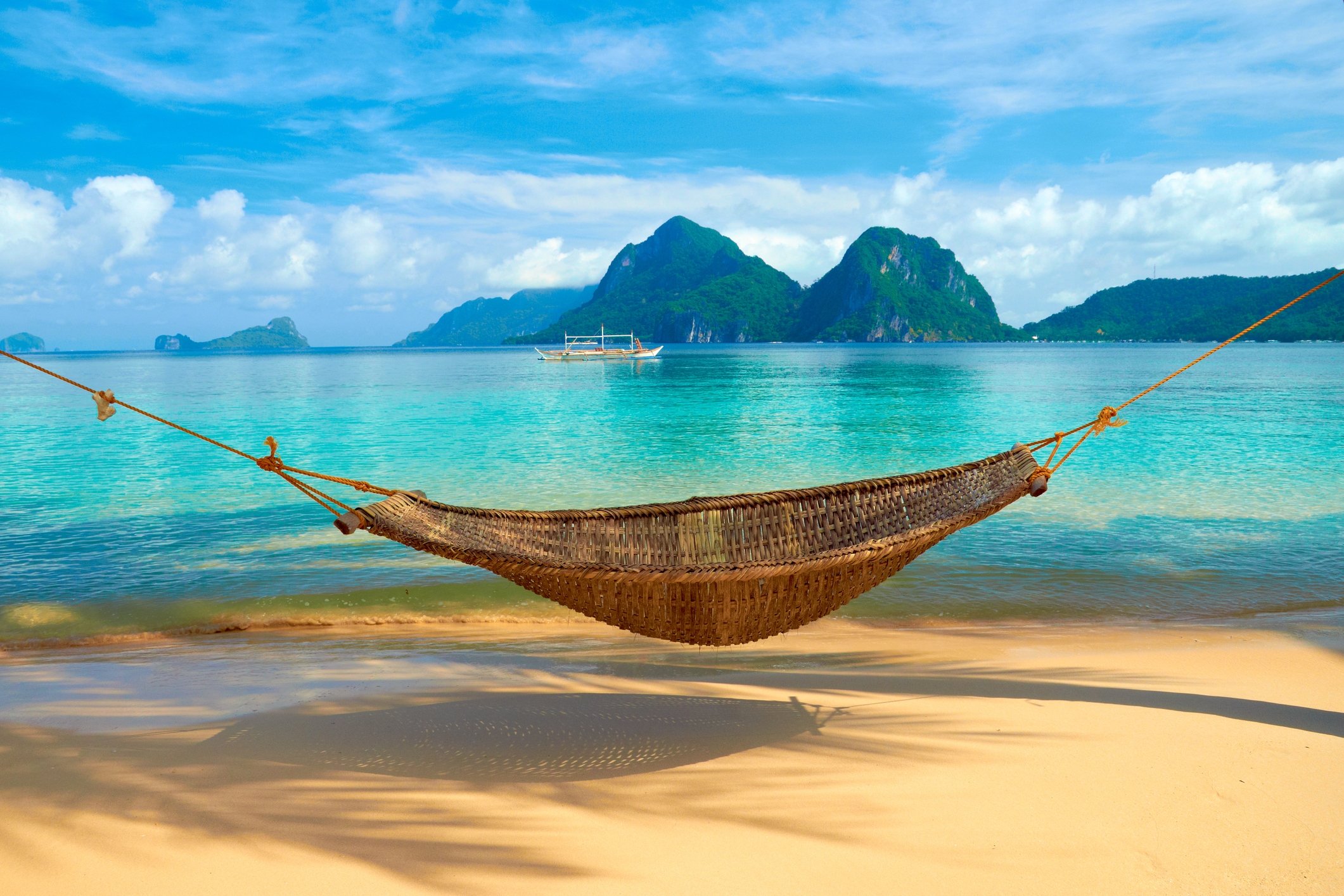 A tropical beach with a hammock strung between two trees.