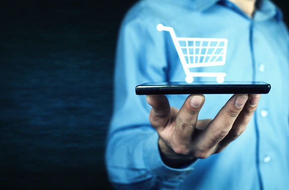 Man holding tablet with digital shopping cart displayed above it.