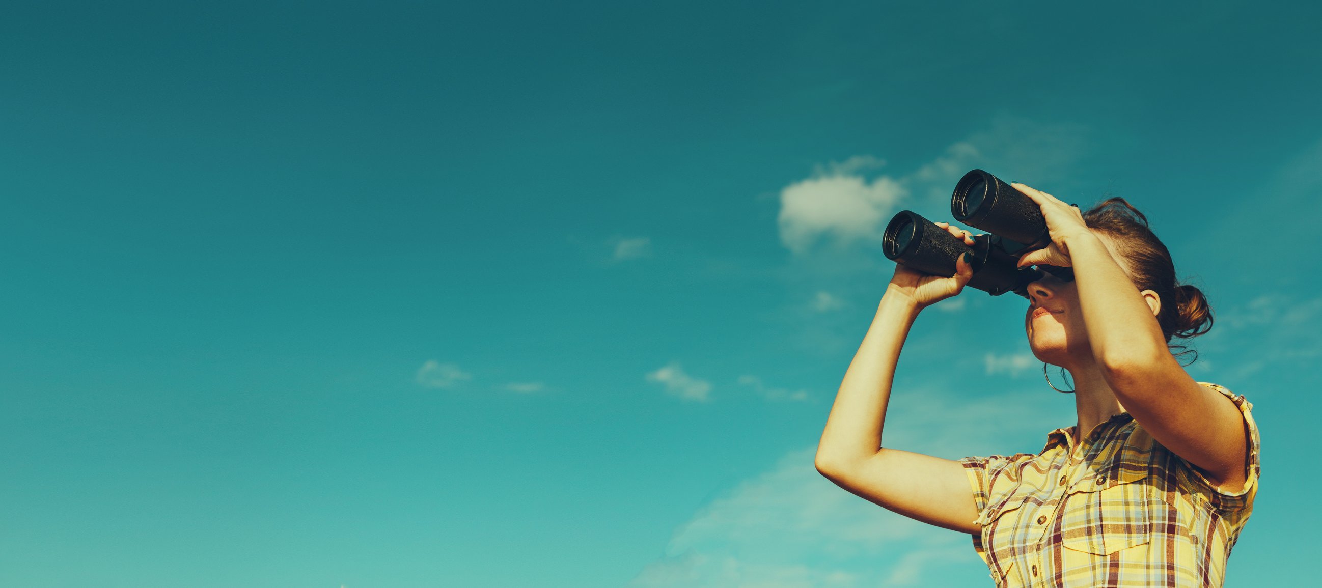 A girl looking through binoculars with a blue sky in the background.