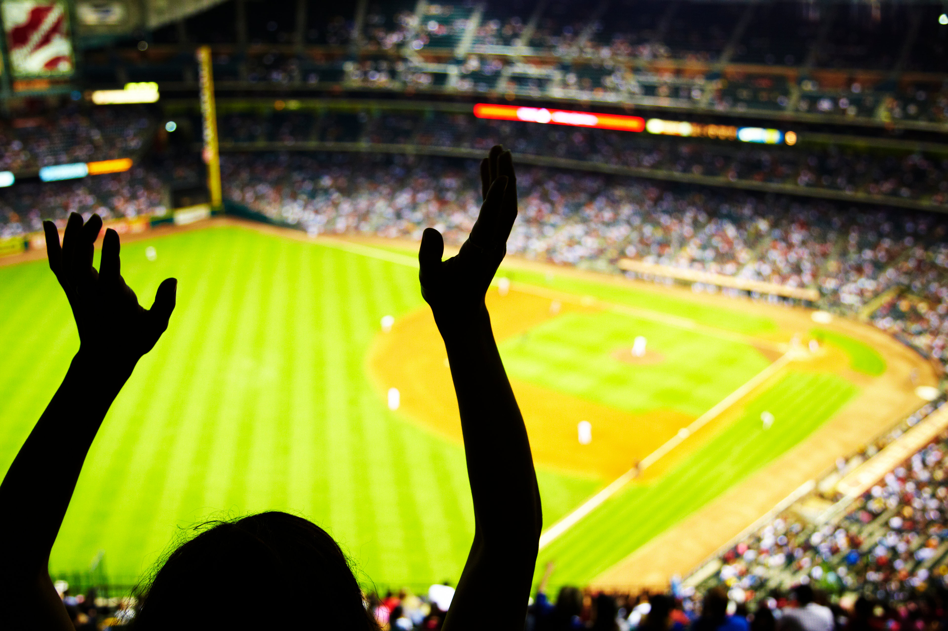 Silhouette of a fan's arms up at a baseball game.