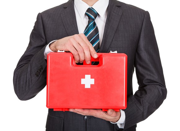 A person in a business suit holding a first aid kit
