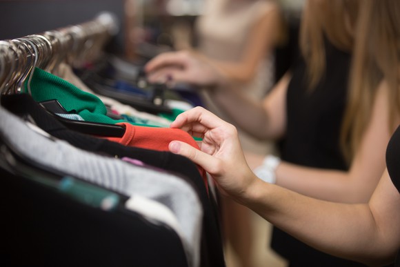 A view of shoppers's hands examining shirts on a store rack.