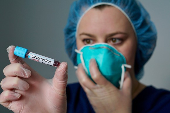 Female healthcare professional with a mask on her face holding a vial with a label stating "Coronavirus"