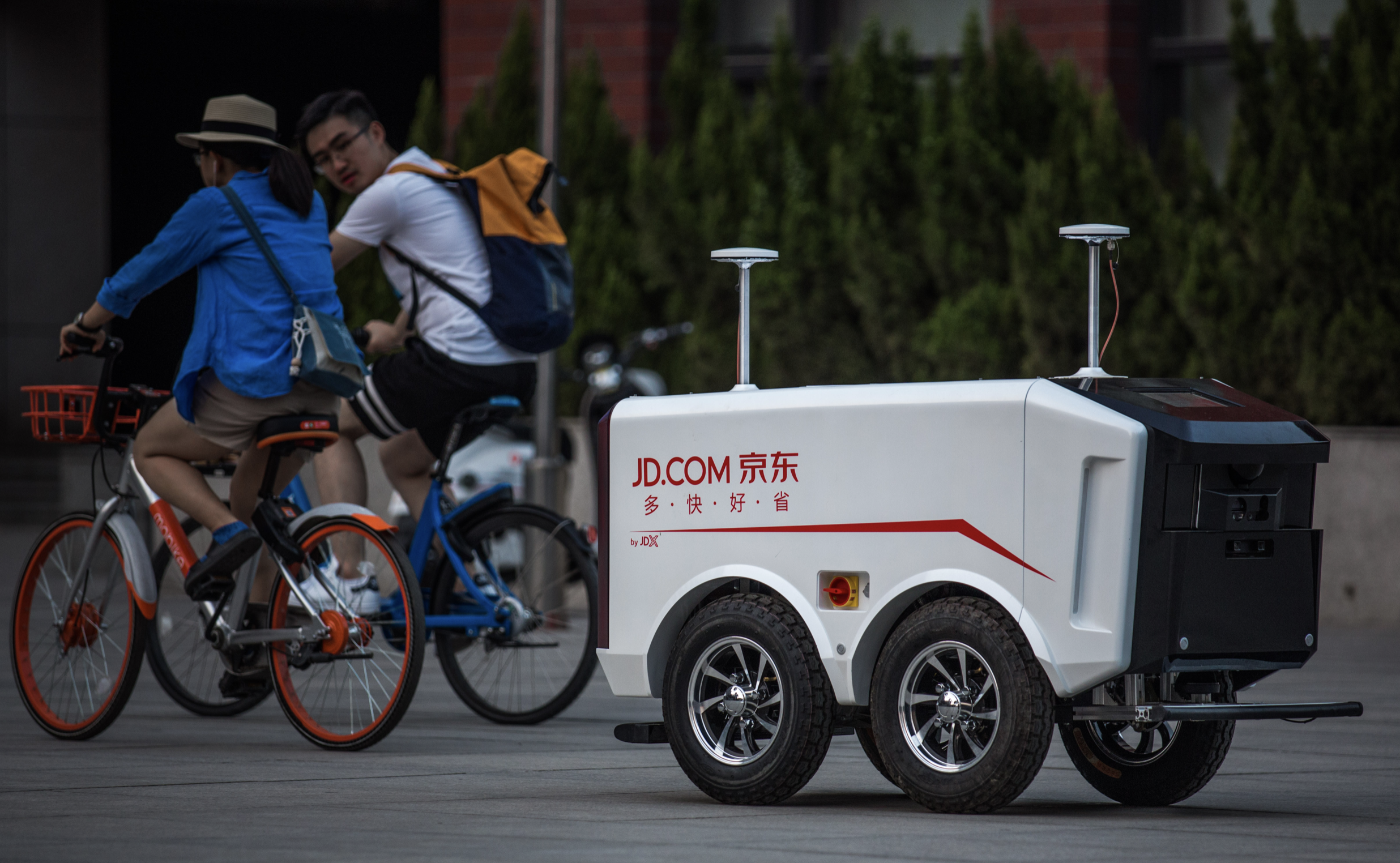 An autonomous delivery bot driving down a street with the JD.com logo displayed on the side.