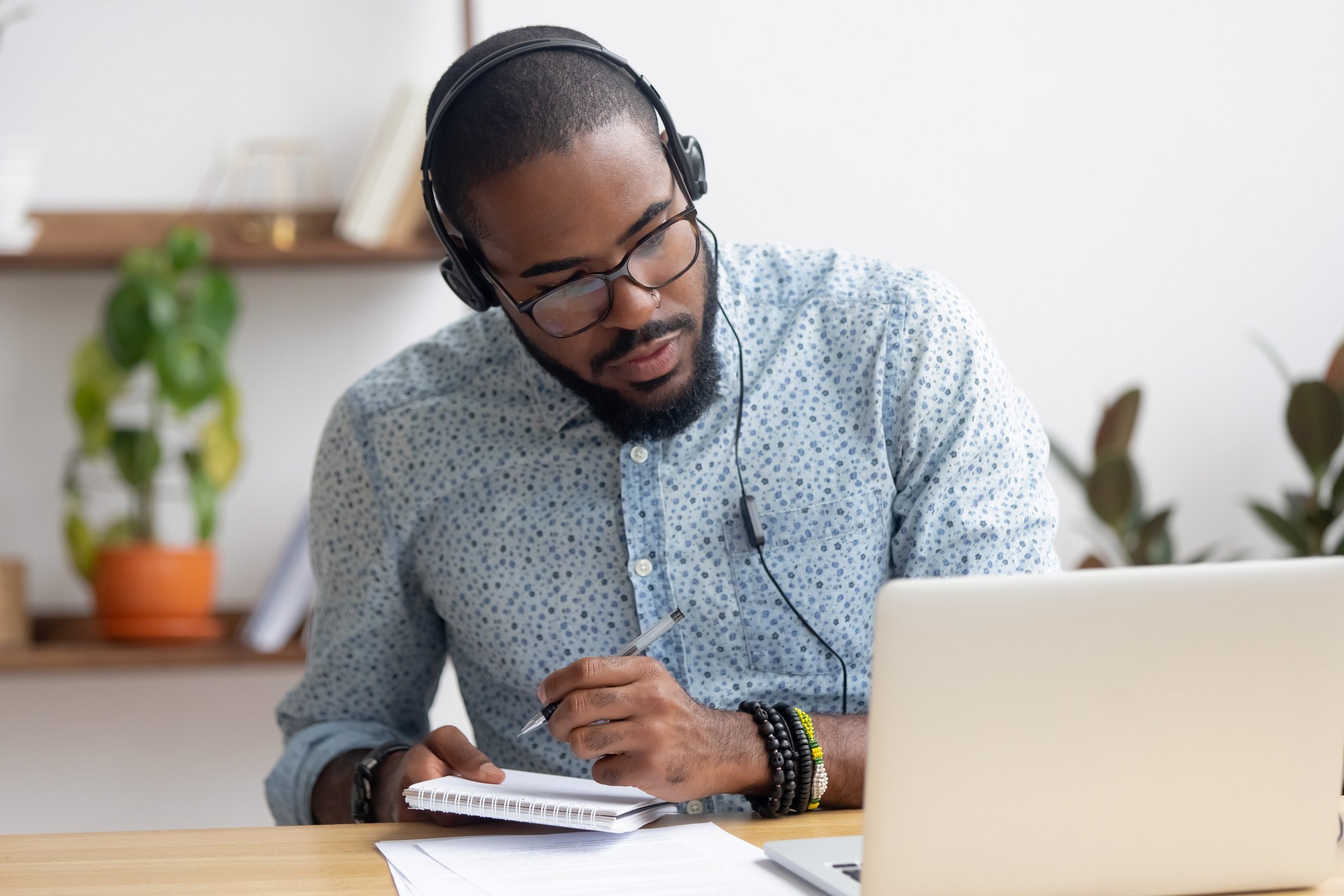 Man with headphones on watching laptop and taking notes