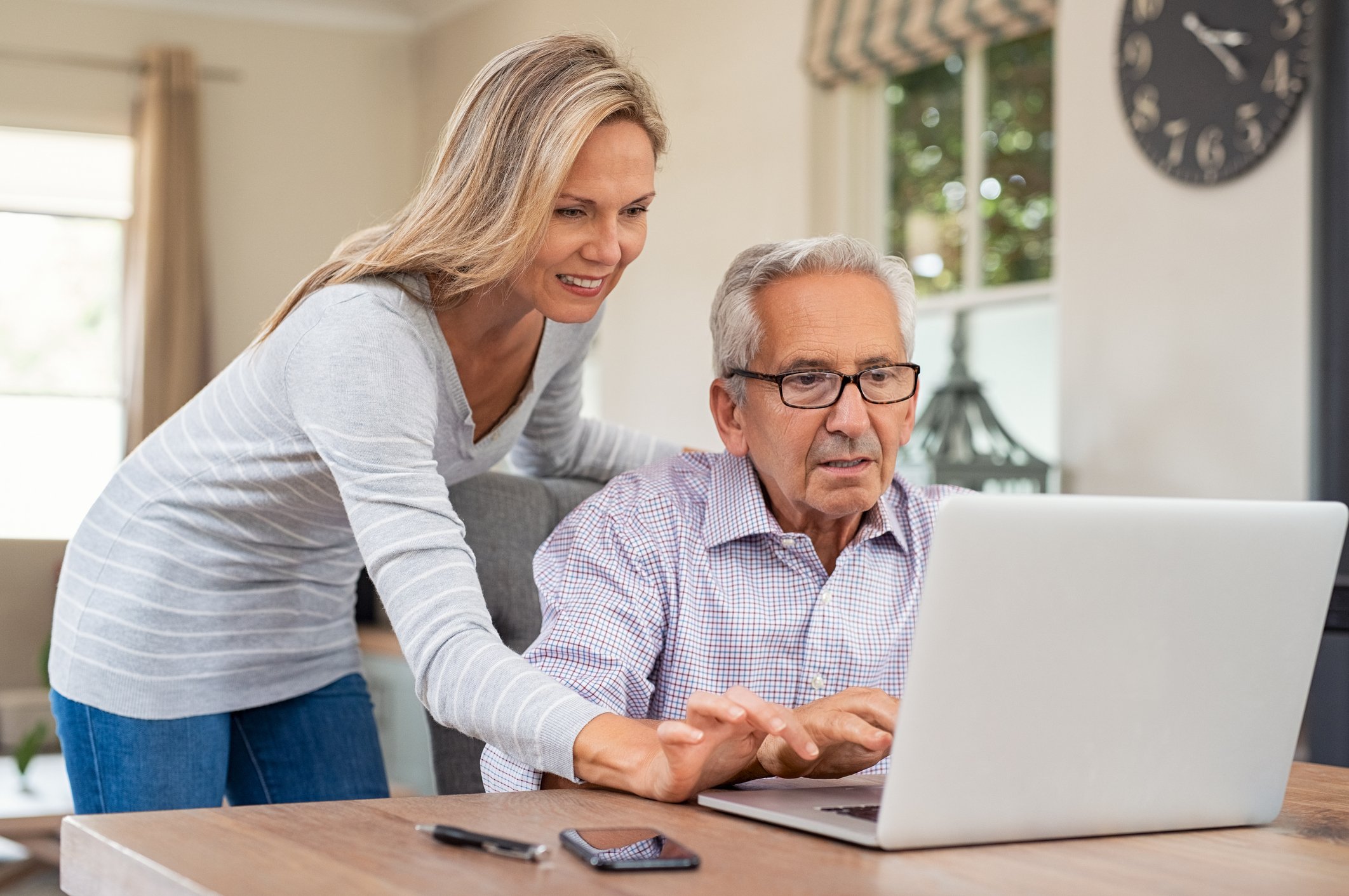 An elderly man uses a laptop as a younger woman looks on.