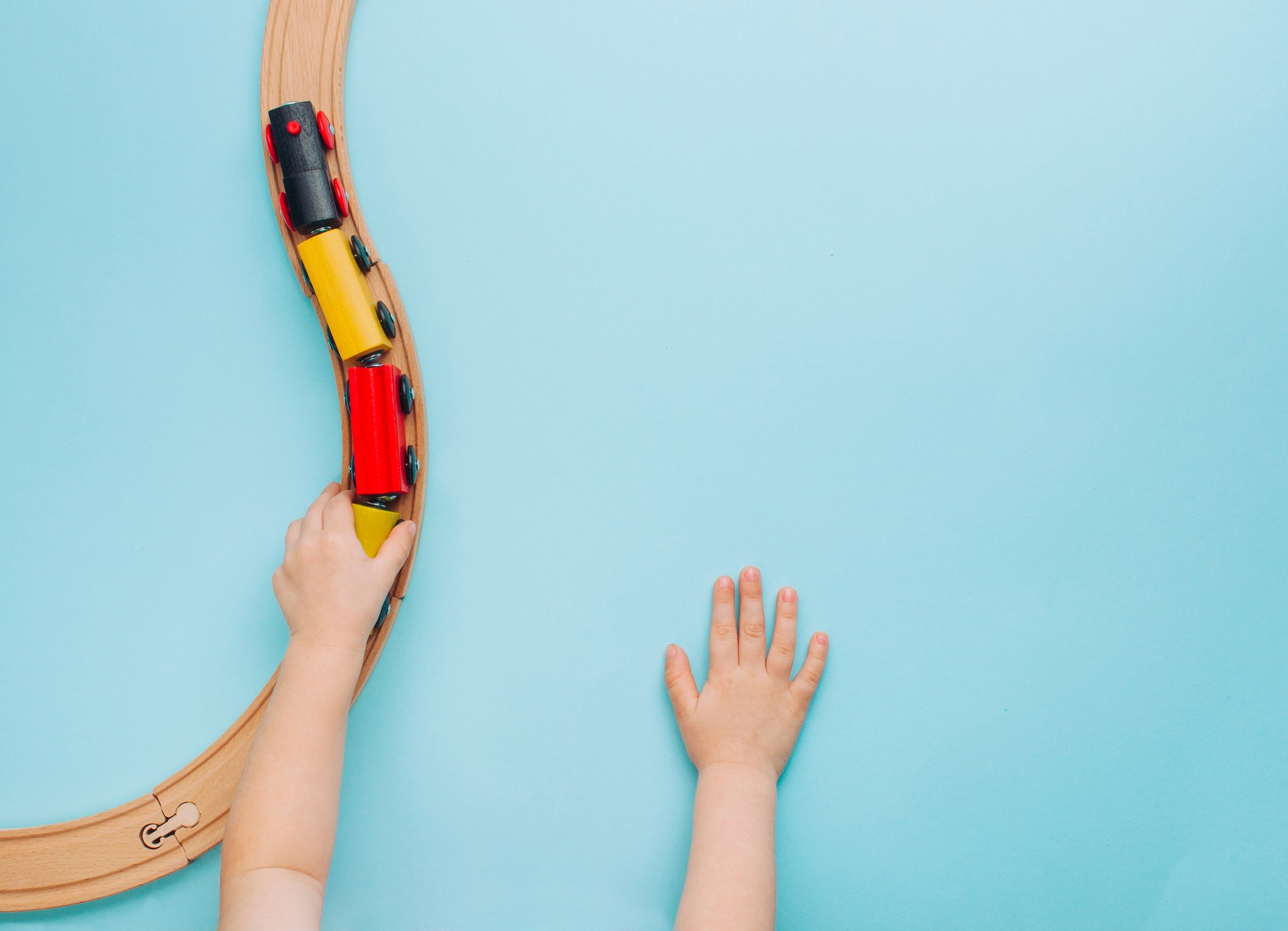 A view of a little boy's hands playing with a toy train is shown against a blue background.