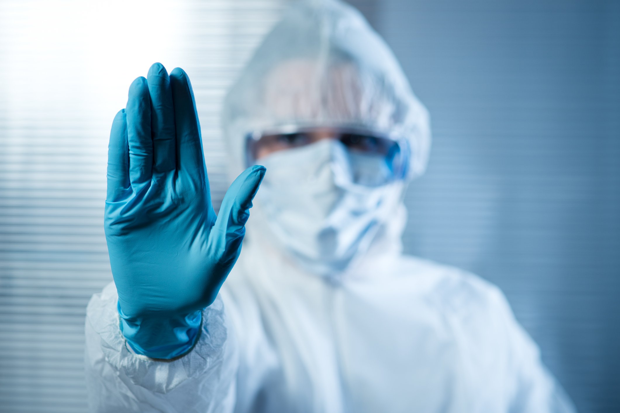 Scientist in hazmat suit raising a gloved hand.