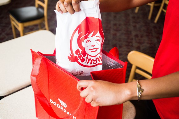 A person puts a Wendy's bag into a Doordash delivery bag.
