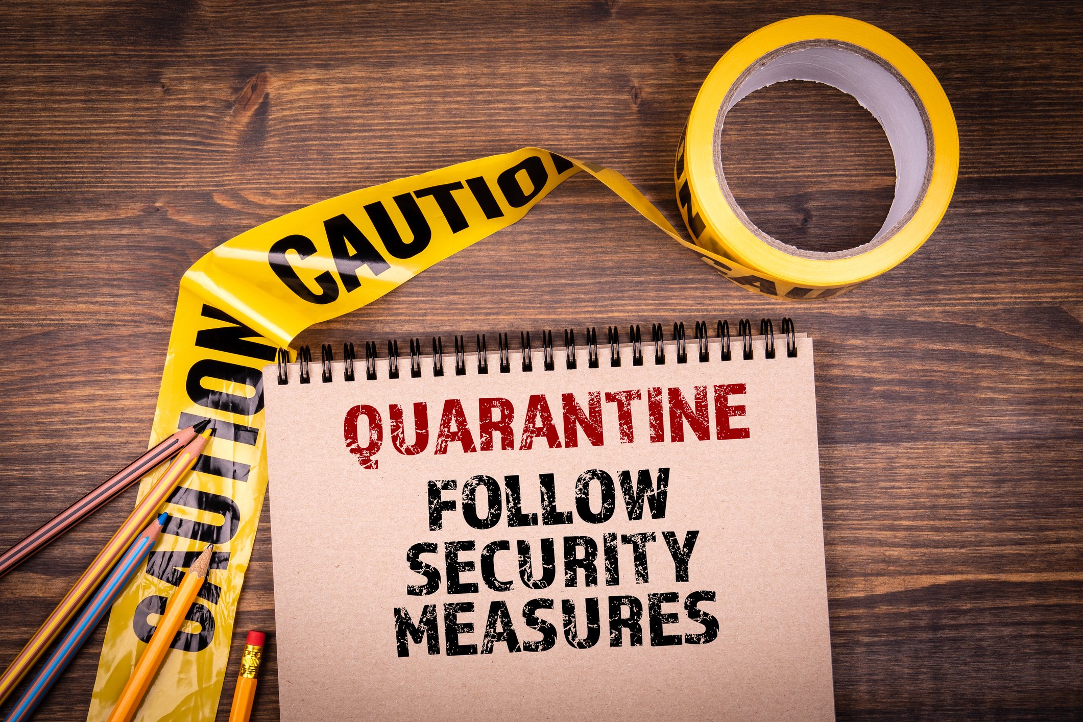 A sign saying Quarantine Follow security measures is shown on a wooden surface near yellow caution tape.