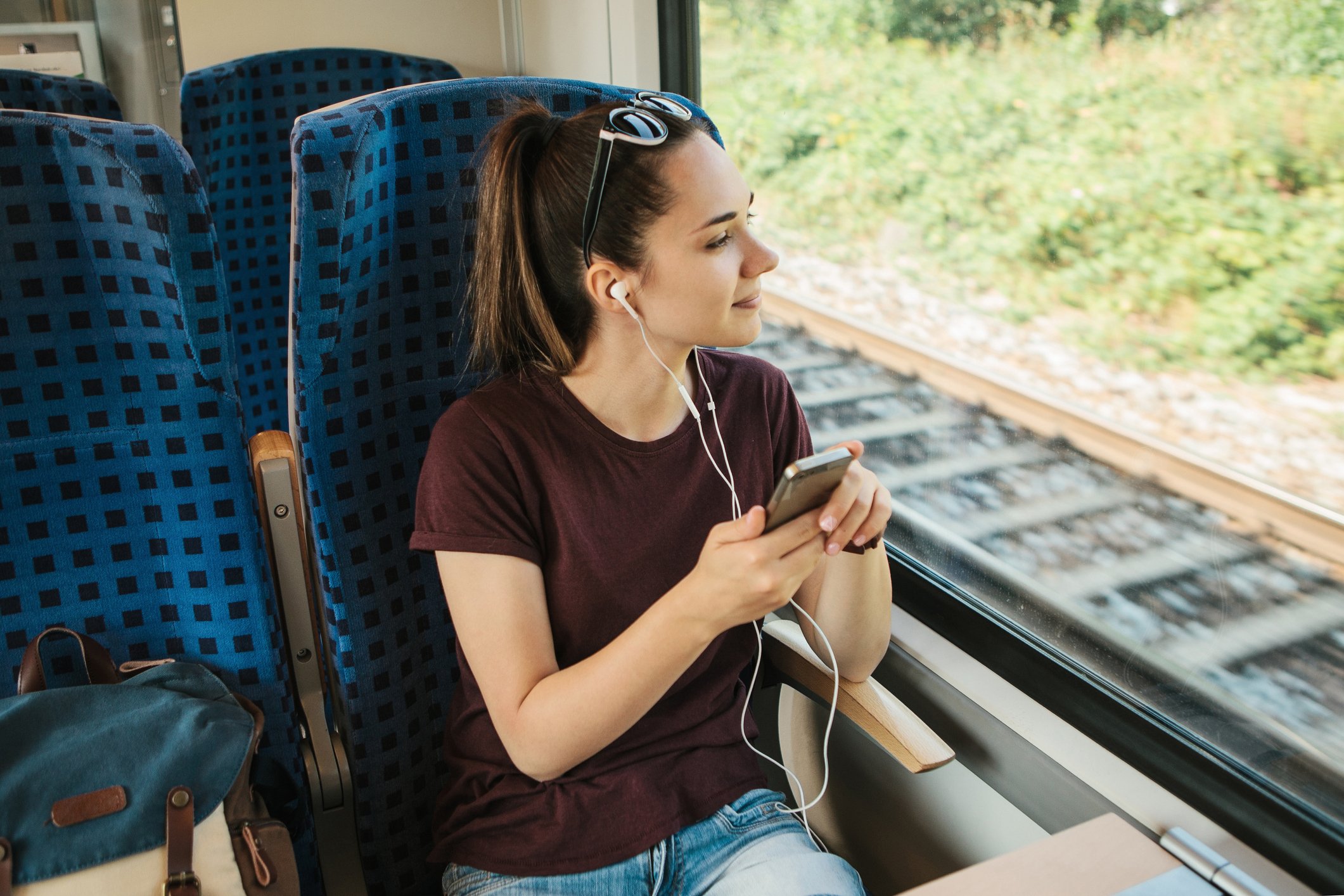 Young woman riding in a train as she listens to something via headphones plugged into her smartphone