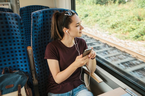 Young woman riding in a train as she listens to something via headphones plugged into her smartphone