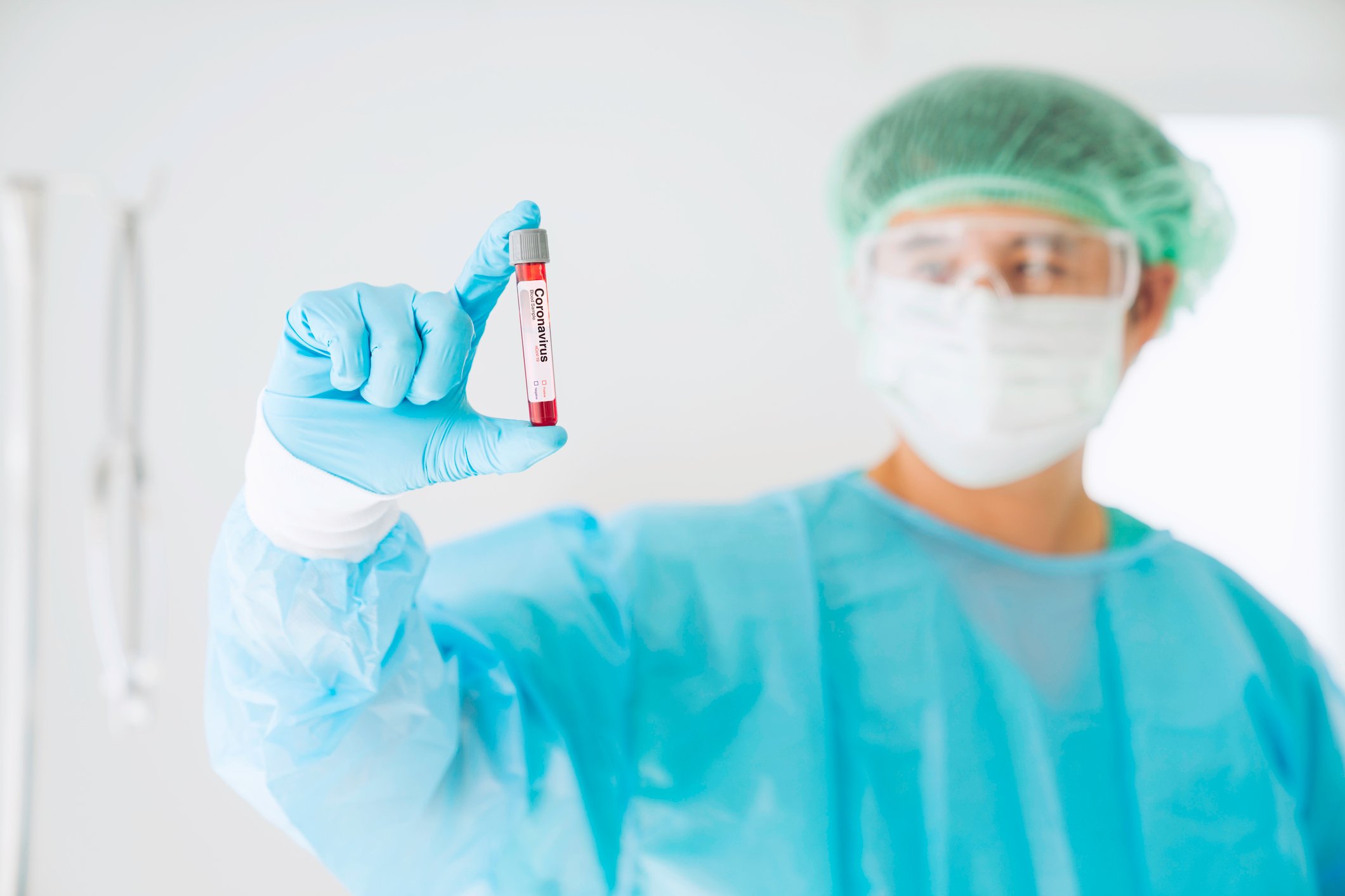 Scientist wearing a mask and safety glasses holding a vial of blood with a label printed on the vial stating coronavirus