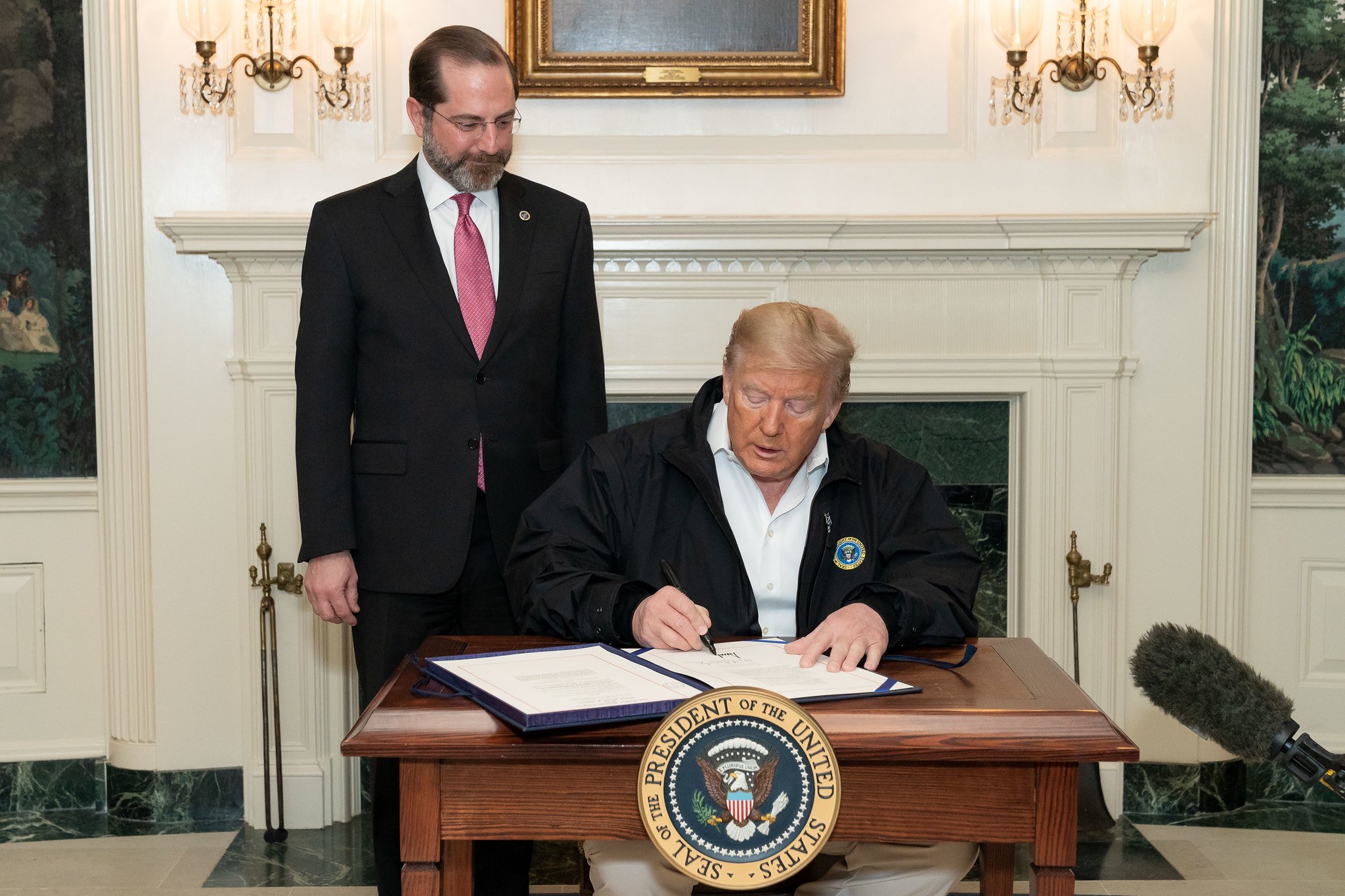 President Tump, flanked by Secretary of Health and Human Services, signs the coronavirus bill into law.