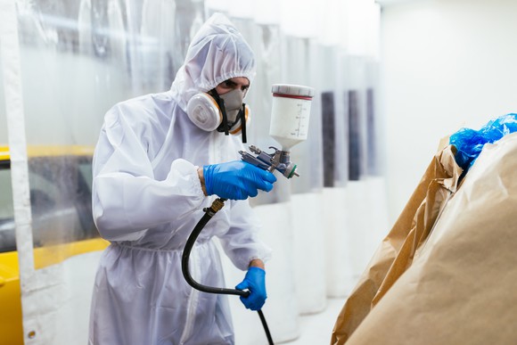 A man with a protective uniform and mask painting a car. 
