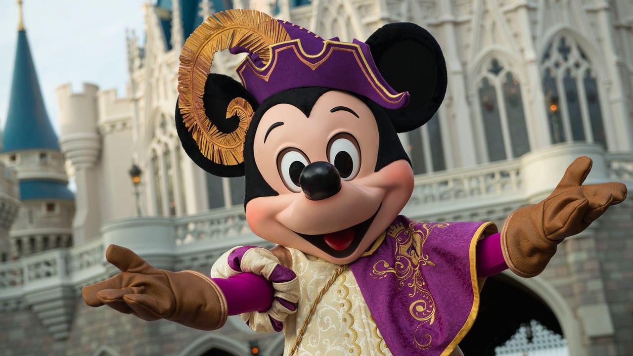 Mickey Mouse in a regal costume in front of Cinderella's Castle