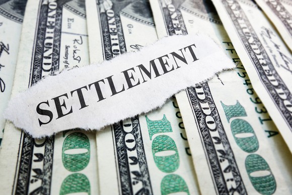 The word settlement typed on a piece of paper lying on top of hundred-dollar bills