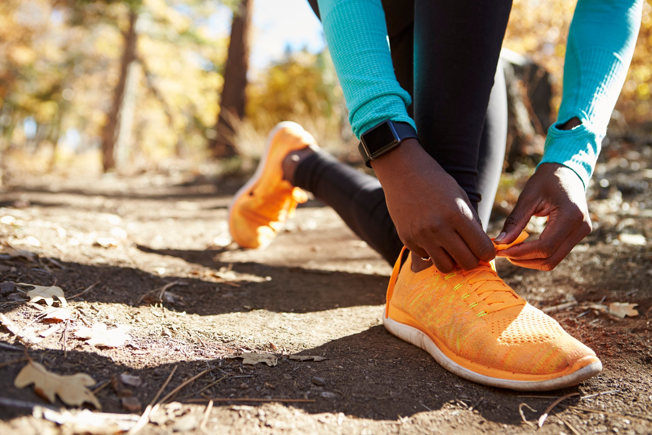 A man wearing a smart watch and tying his sneakers on a trail.