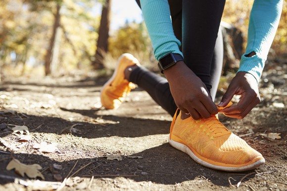 A man wearing a smart watch and tying his sneakers on a trail.