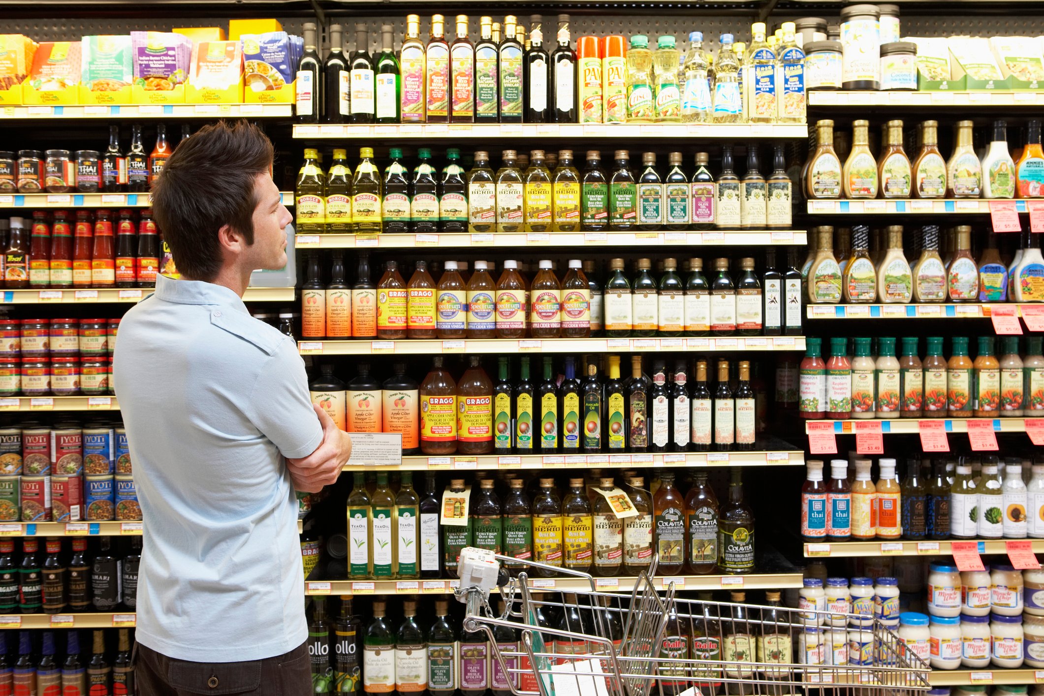 Man looking at sauces, oils, and salad dressing in a grocery store aisle. 
