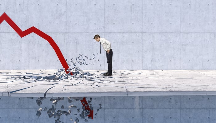 A businessman leans over to watch as a huge red arrow crashes through the floor by his feet.