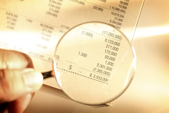 A person holding a magnifying glass looking at figures on a financial statement.