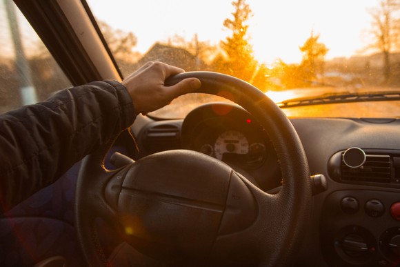 Man steering a car as sun sets