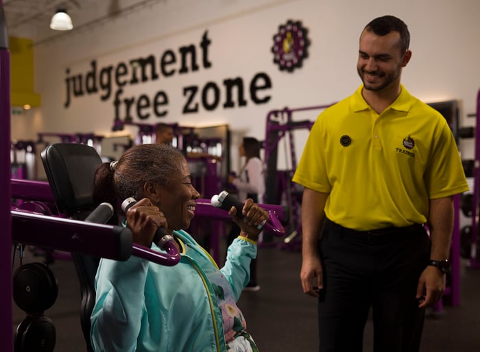 A Planet Fitness trainer smiles at a woman who is working out.