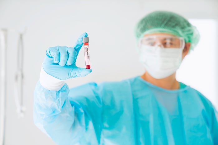 Scientist wearing a mask and safety glasses while holding a vial of blood with a label in the vial that has coronavirus printed on it