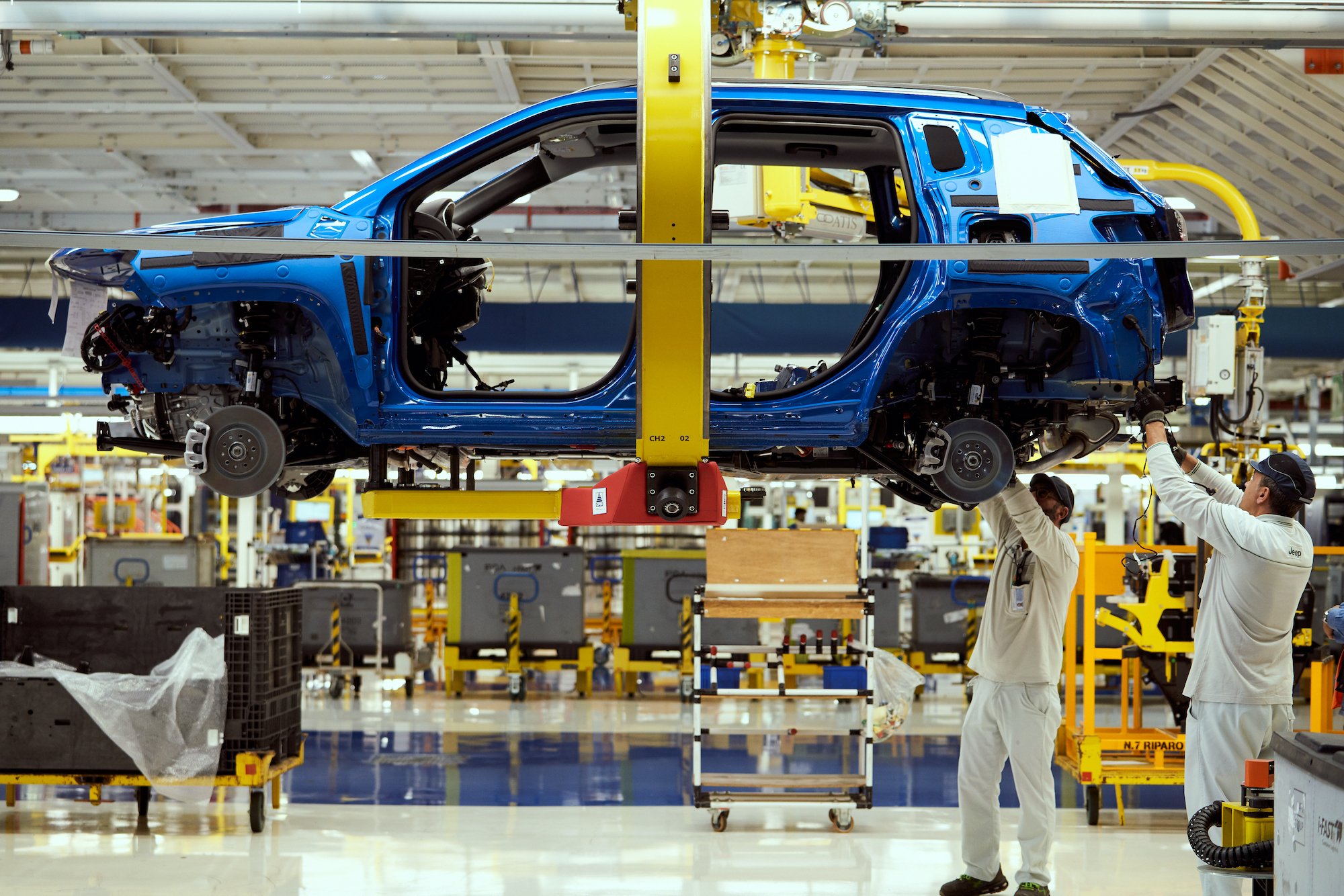 A partially-assembled blue Jeep Compass, a compact SUV, on a factory assembly line.