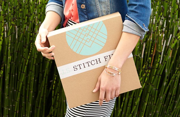 A woman is holding a package with the Stitch Fix logo. 