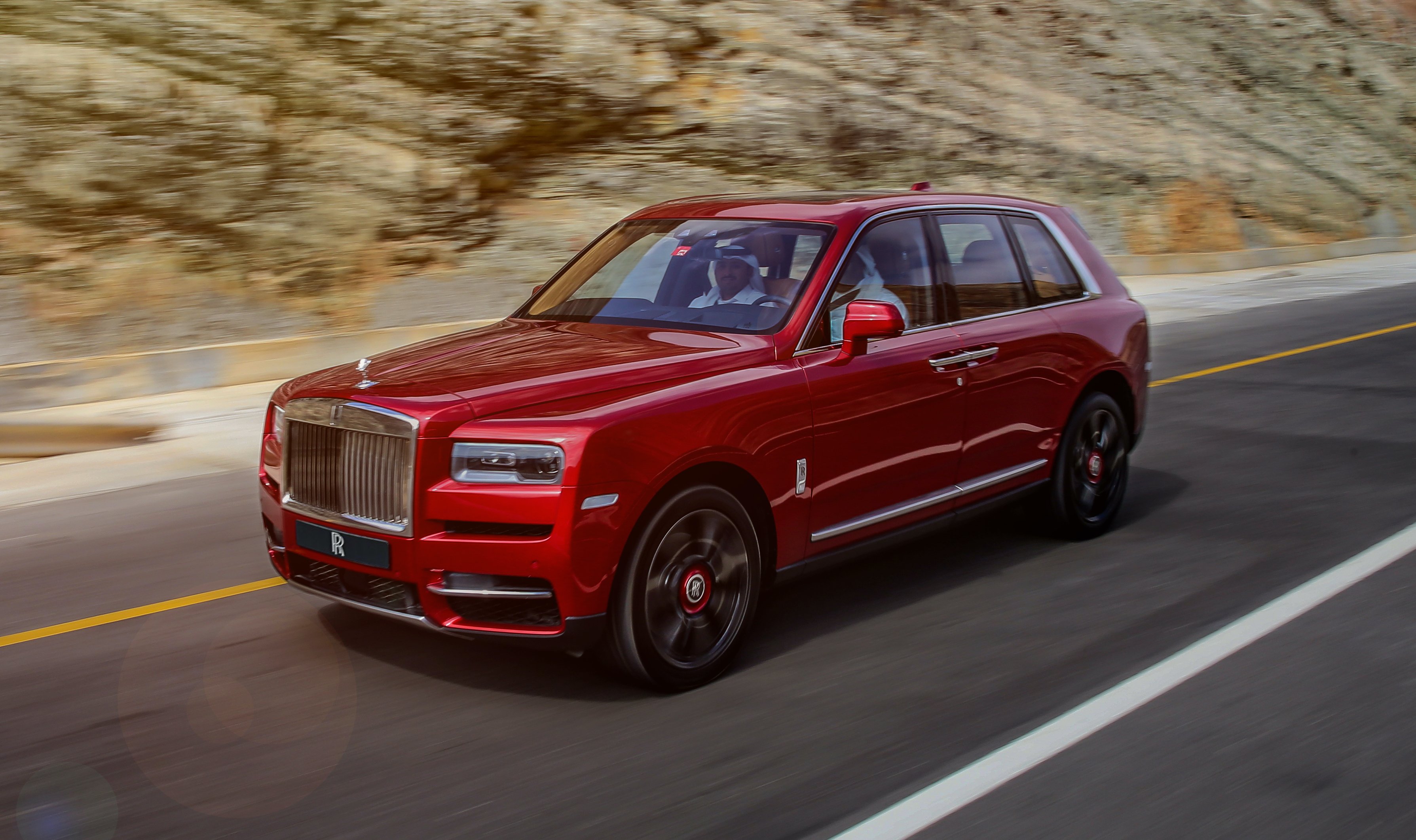 A red Rolls-Royce Cullinan, an ultra-luxury SUV, on a mountain road.
