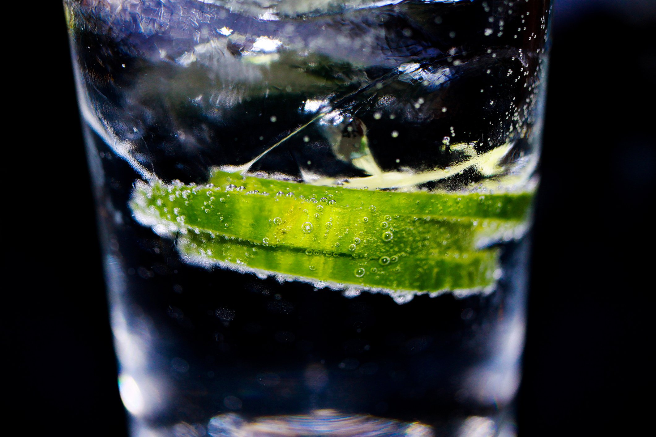 A close-up photo of a gin and tonic drink is shown against a black background.