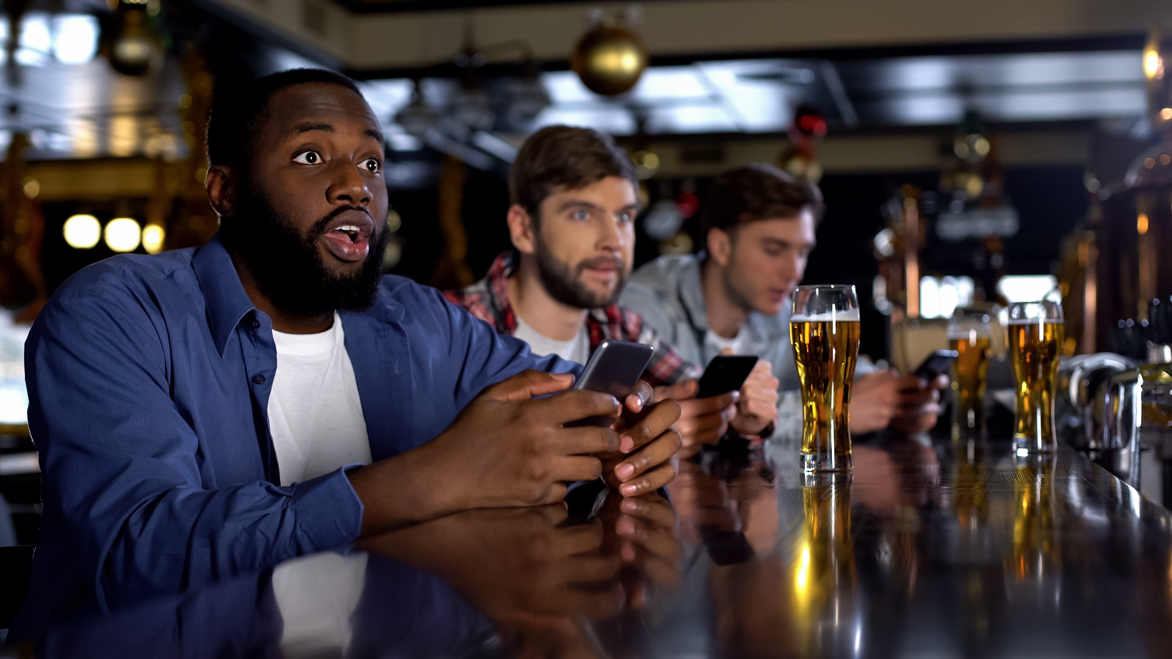 In a bar, men watching sports wager using online apps