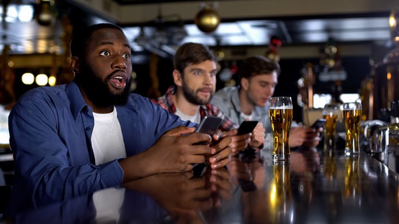 In a bar, men watching sports wager using online apps