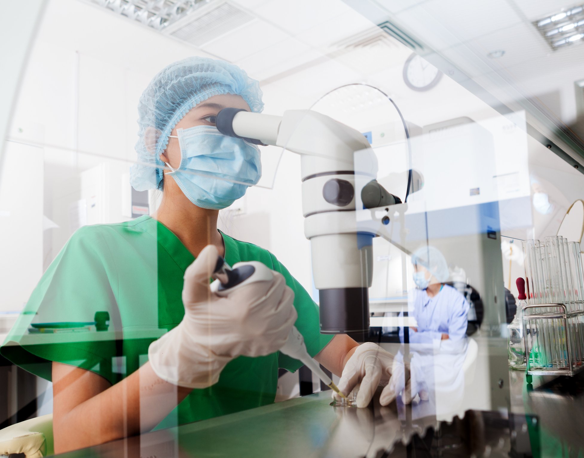 A biotech lab researcher using a pipette tool to place samples under a microscope.