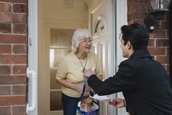 A young smiling delivery boy delivers groceries to a senior citizen. 