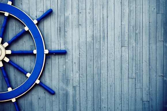 A blue vintage yacht helm wheel lies on a wooden deck.
