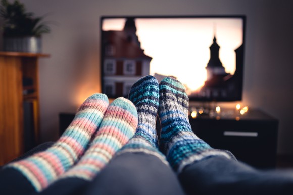 Two pairs of feet with socks, in front of a television.