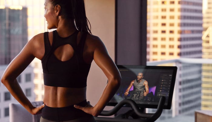 A woman working out on a Peloton bike takes a break to admire the skyline outside.