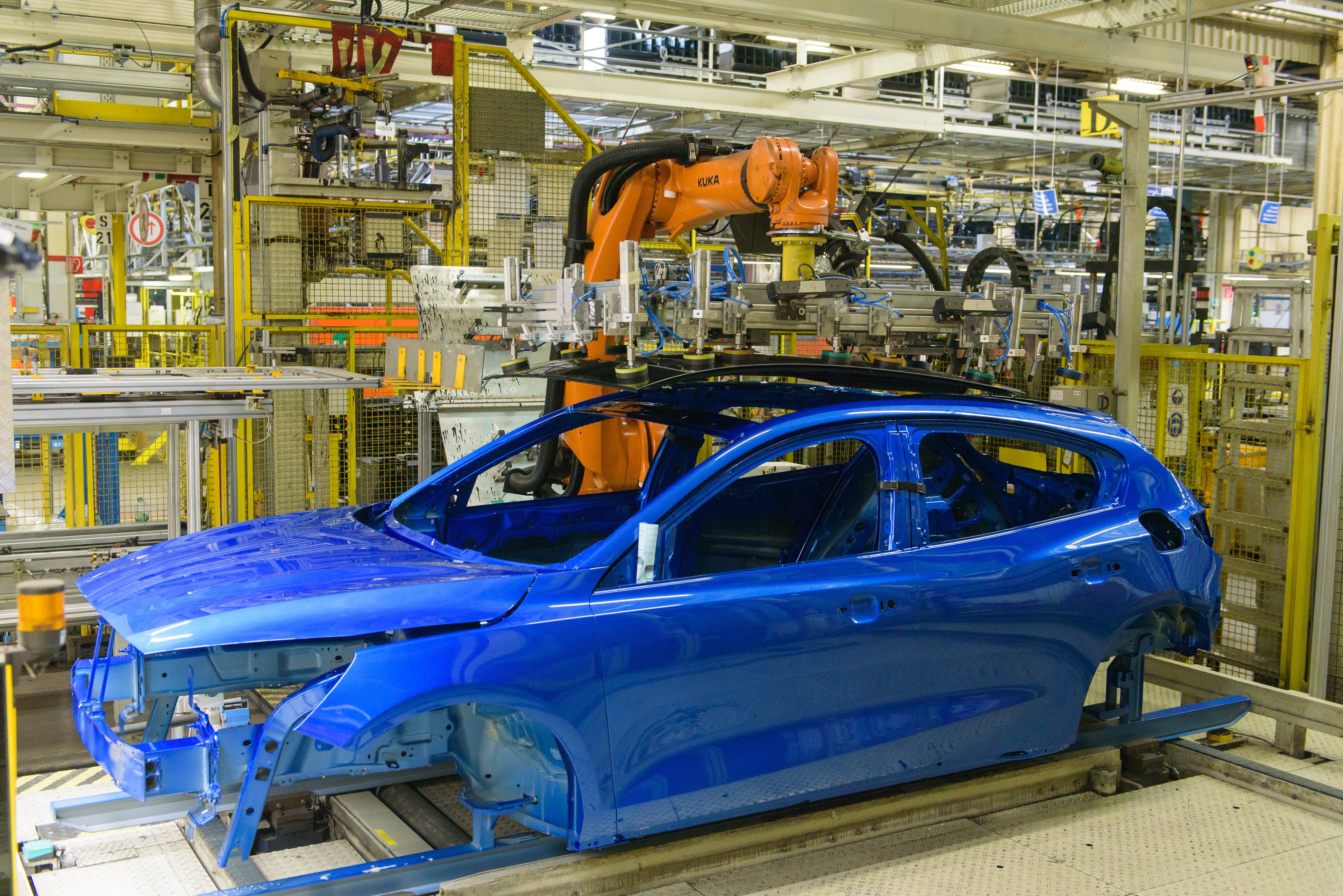 A partially assembled blue Ford Focus, a compact hatchback, surrounded by manufacturing robots.