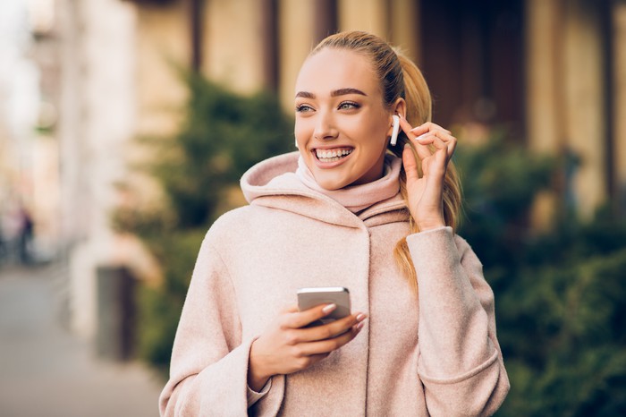 A woman holding her smartphone and adjusting her wireless headphones. 